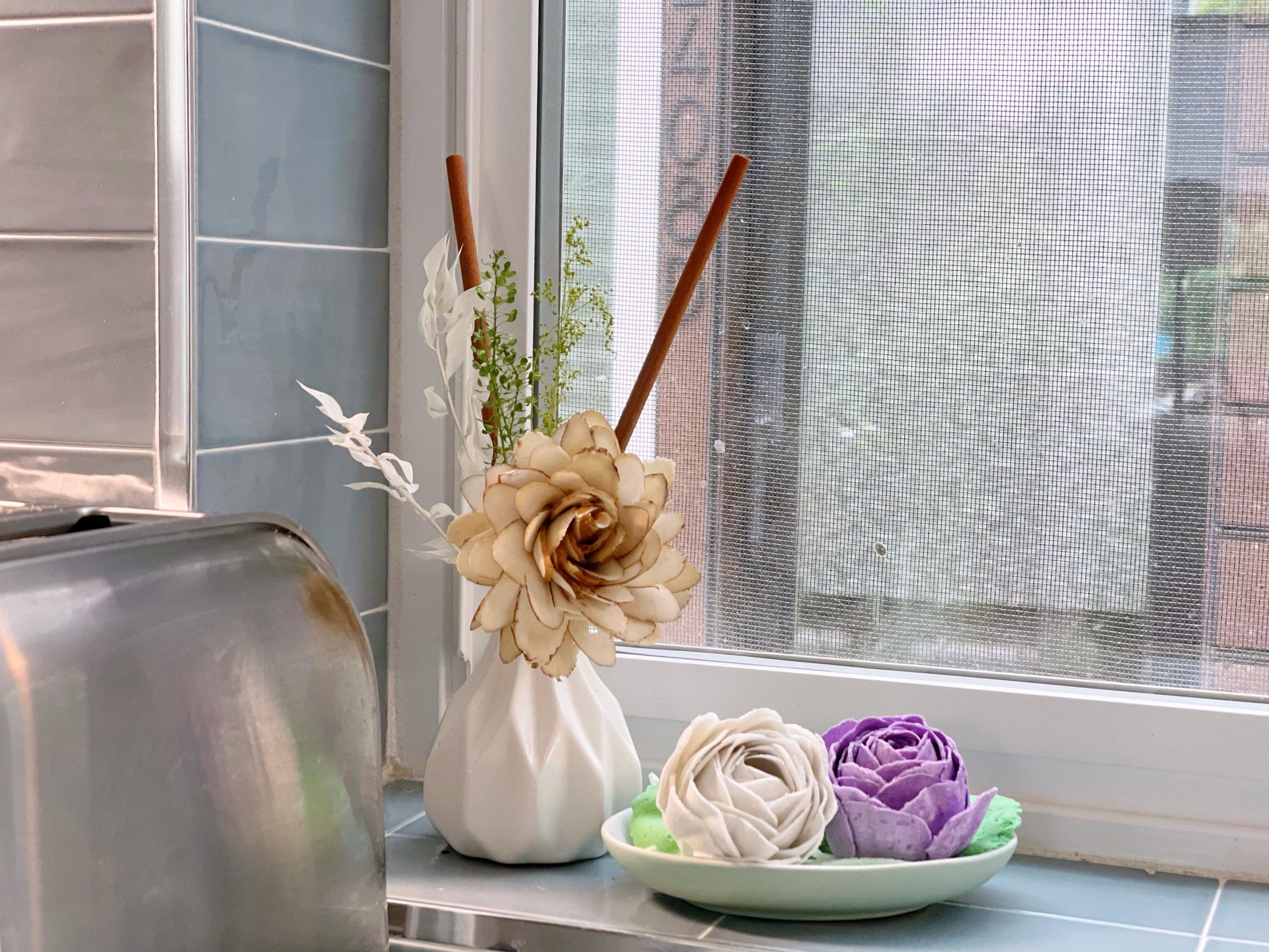Kitchen windowsill with decorative flowers in a vase and dish, next to a toaster.