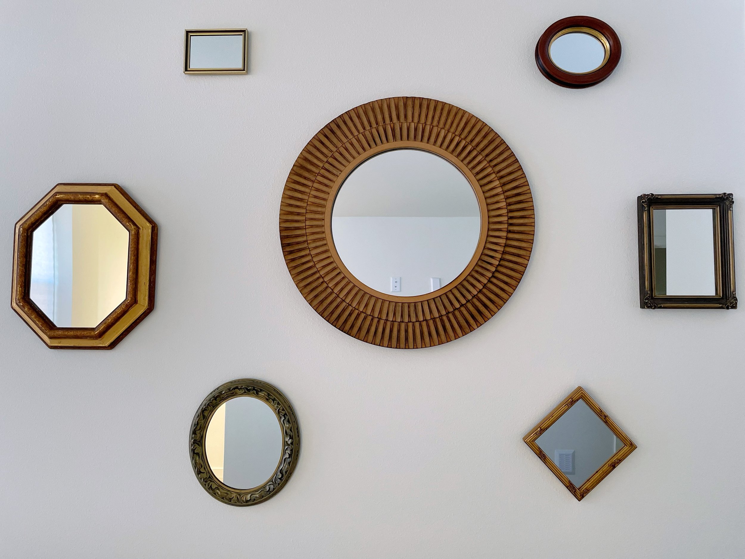 A wall with various decorative mirrors in different shapes and frames.
